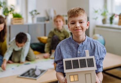 Petit garçon posant avec un modèle de maison avec système solaire pendant une leçon scolaire.